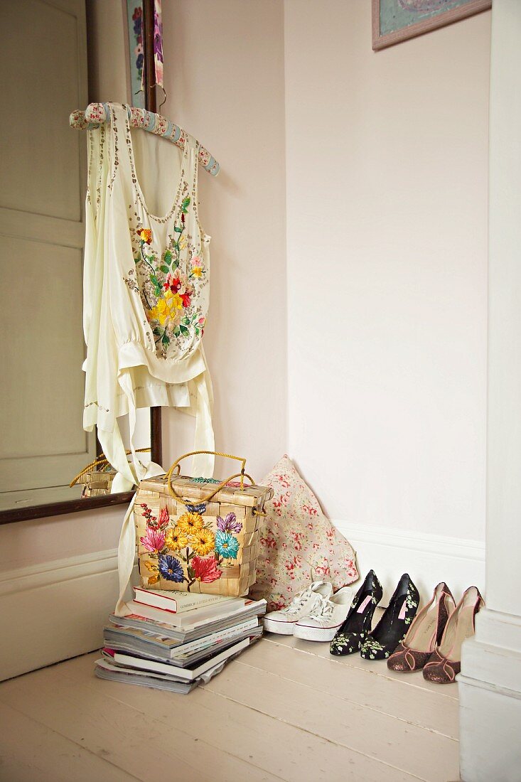High-heeled shoes next to stack of books and embroidered top on coat hanger in corner of room