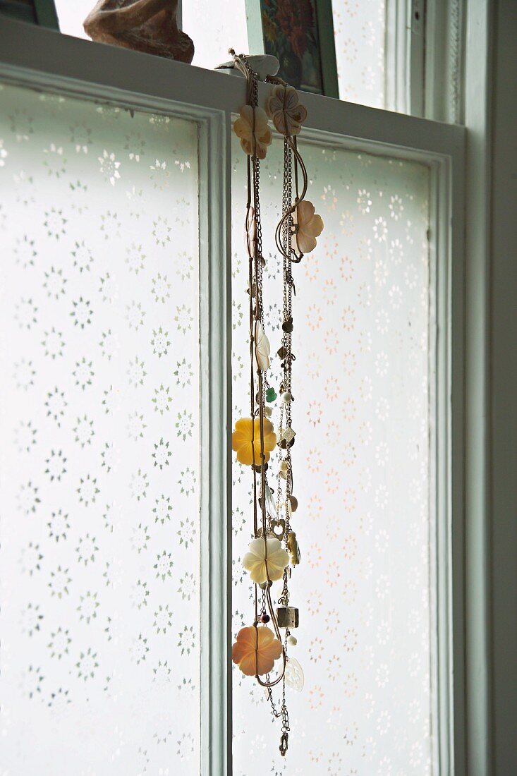 Halskette mit Blumenmotiven vor Fenster hängend