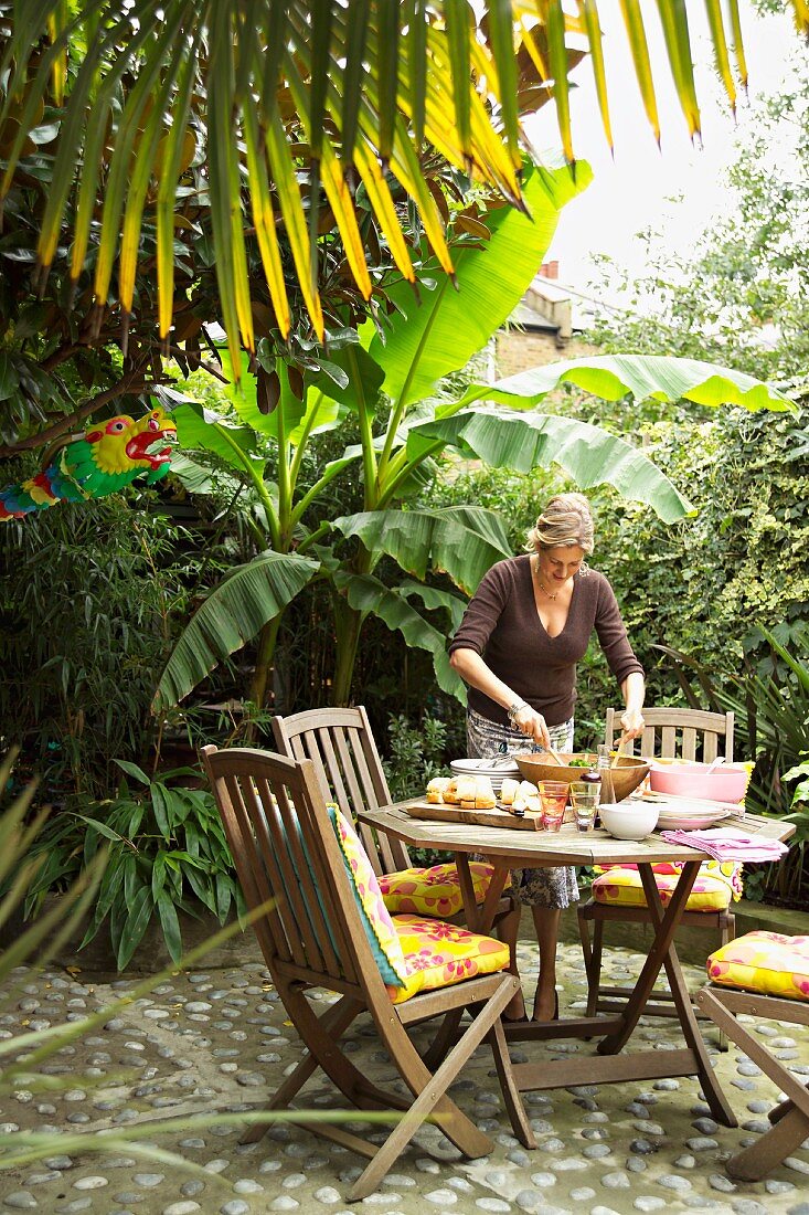 Frau bereitet Essen auf Terrassentisch vor in tropischer Umgebung