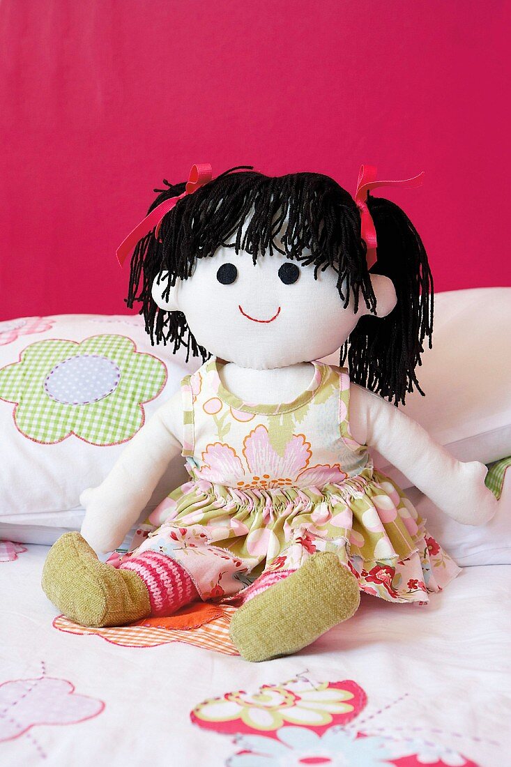 Hand-made rag doll with black wool pigtails against bright pink wall