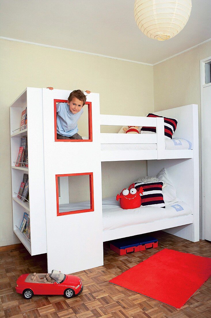 Weisses Stockbett mit Spielfenstern und integriertem Bücherregal in einem Kinderzimmer