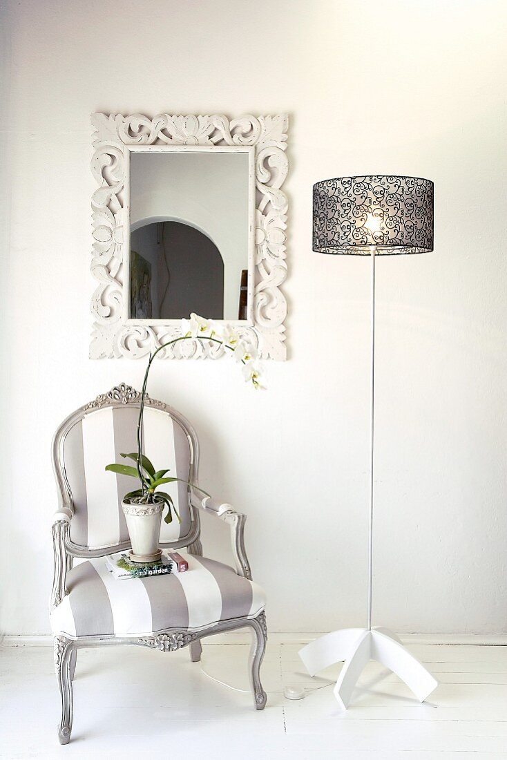 Gepolsterter Stuhl im Vintagelook neben Designerlampe vor Wand mit Spiegel