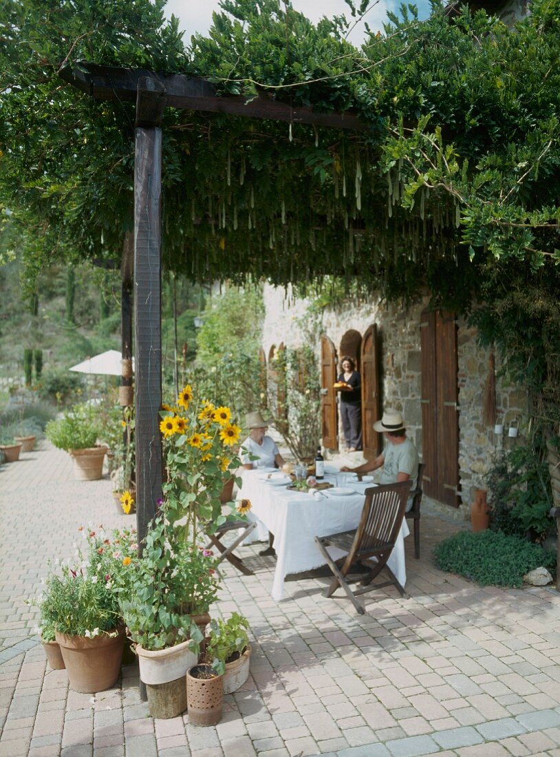 Kaffeepause auf Terrasse mit bewachsener Pergola vor mediterranem Landhaus