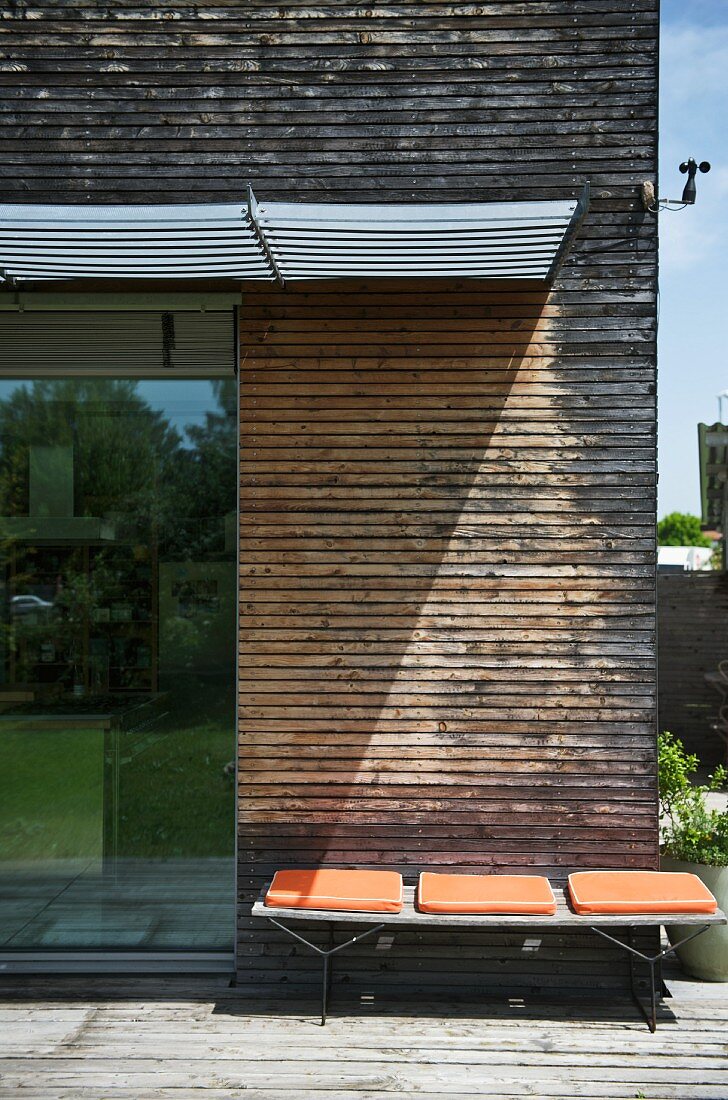 Simple bench with orange cushions against wooden wall