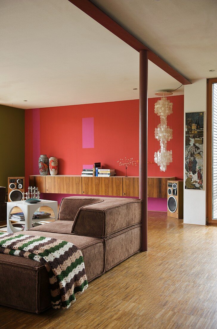 Wohnraum im Retrolook mit braunem Polstersofa und Sideboard an rot getönter Wand