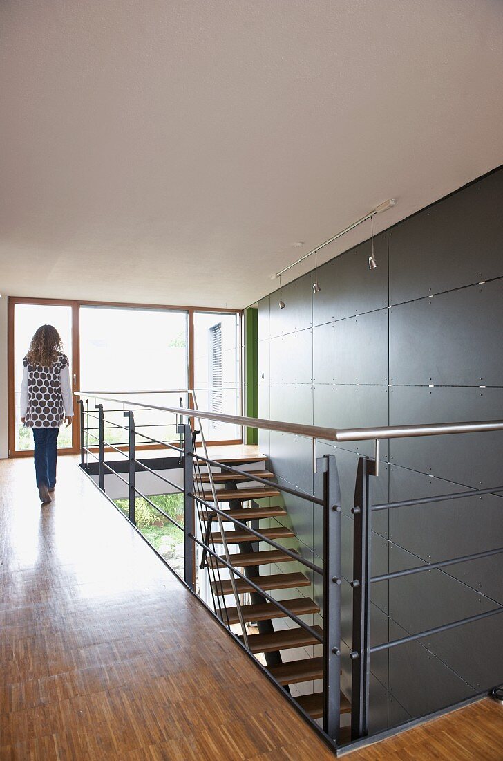 Jugendliche läuft auf Galerie mit Treppenabgang vor Wand und grauen Fliesenplatten