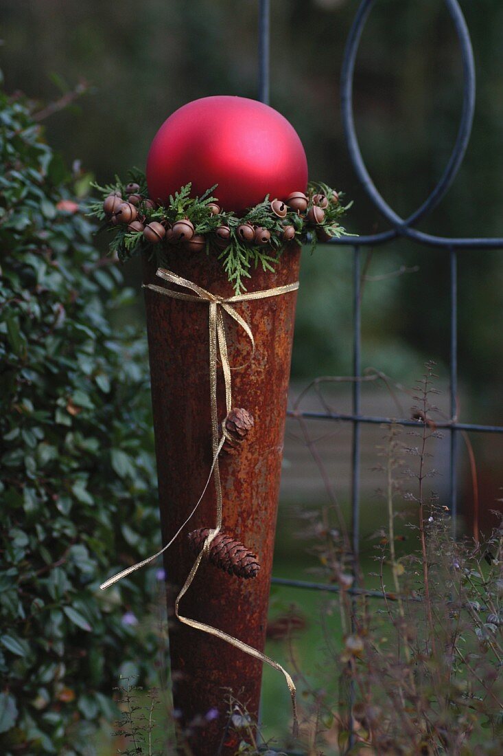 Rusty cone topped with large, red bauble framed with a wreath of thuja twigs and bells