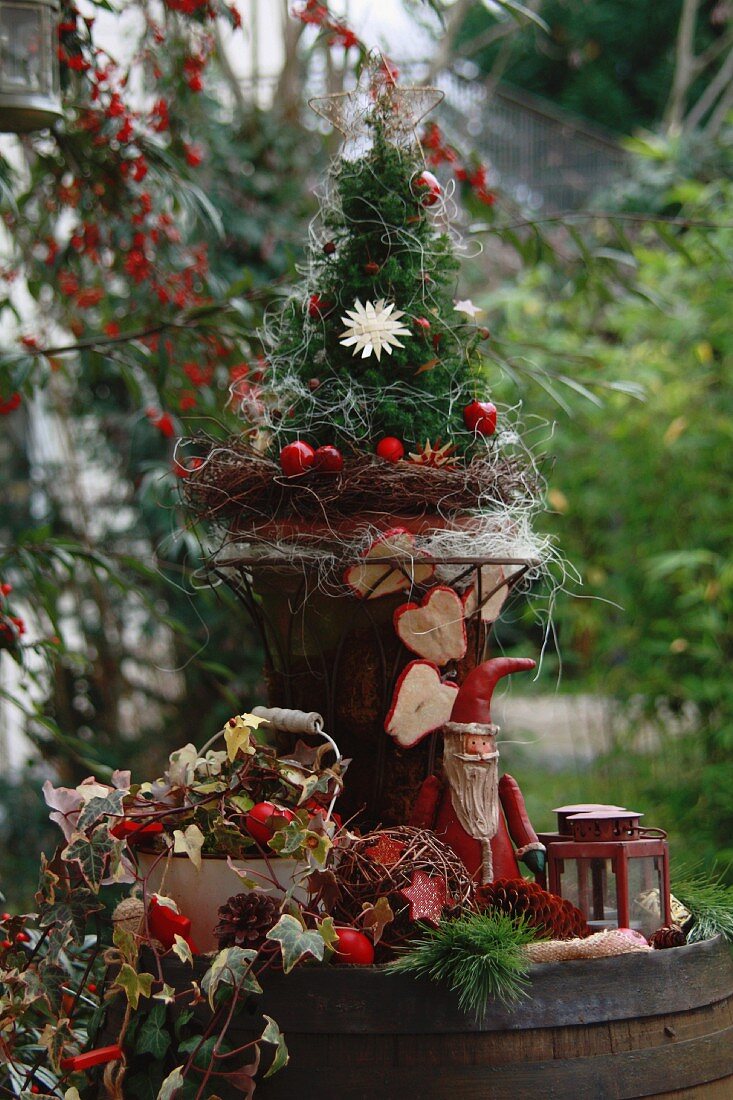 Altes Holzfass mit kleinem Tannenbaum, Efeu, Äpfeln, Weihnachtsmann und Laternen dekoriert