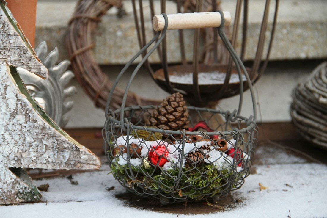 Wire basket with pine cones and baubles in snow