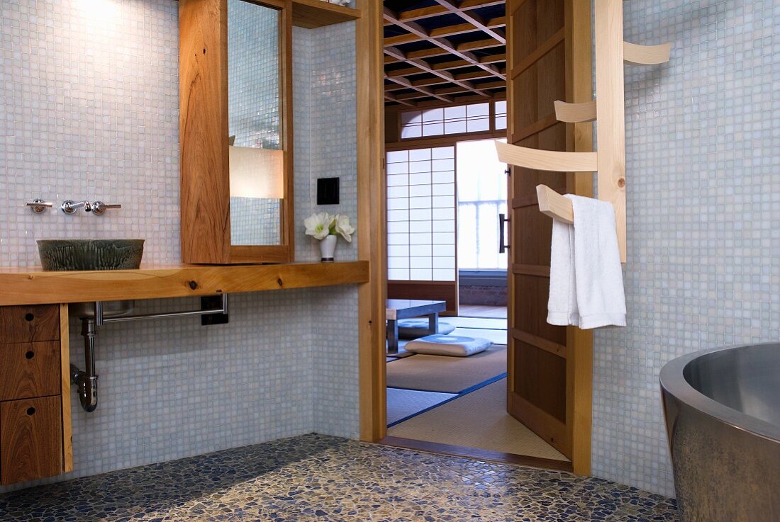 Schlichtes Bad mit Mosaikfliesen an Wand und Holzeinbauten mit offener Tür und Blick in Schlafraum in japanischem Stil
