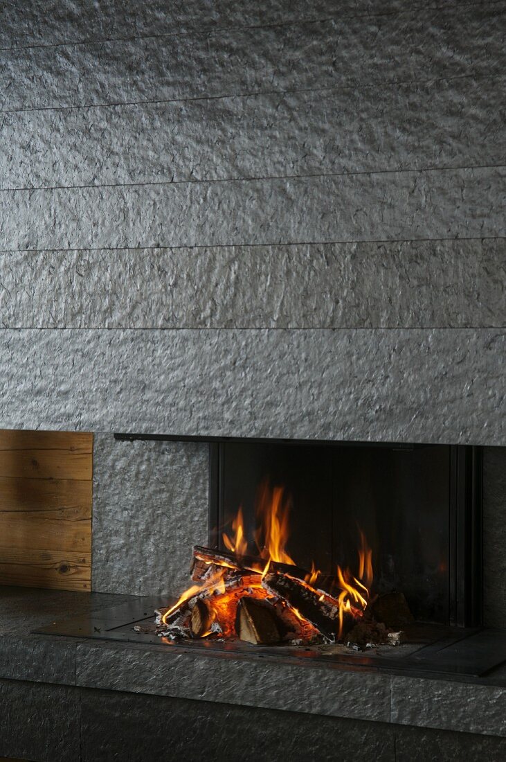 Blazing fire in open fireplace clad in dark grey stone slabs