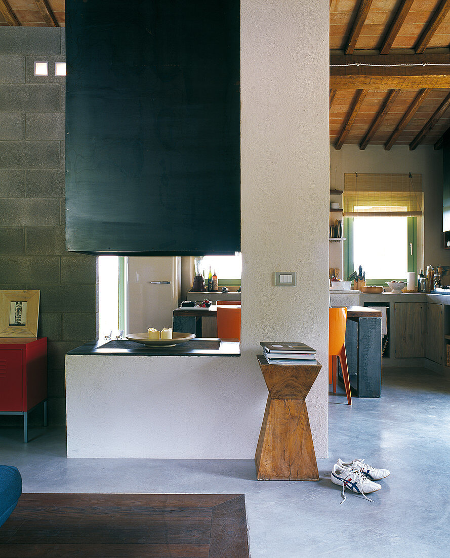 Open-plan interior in shades of green and blue below roof structure with terracotta tiles; open fireplace in centre