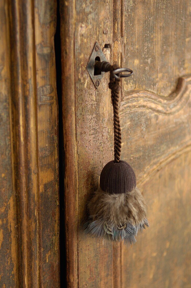 Schlüsselanhänger mit Vogelfedern an alter, ramponierter Landhaustür