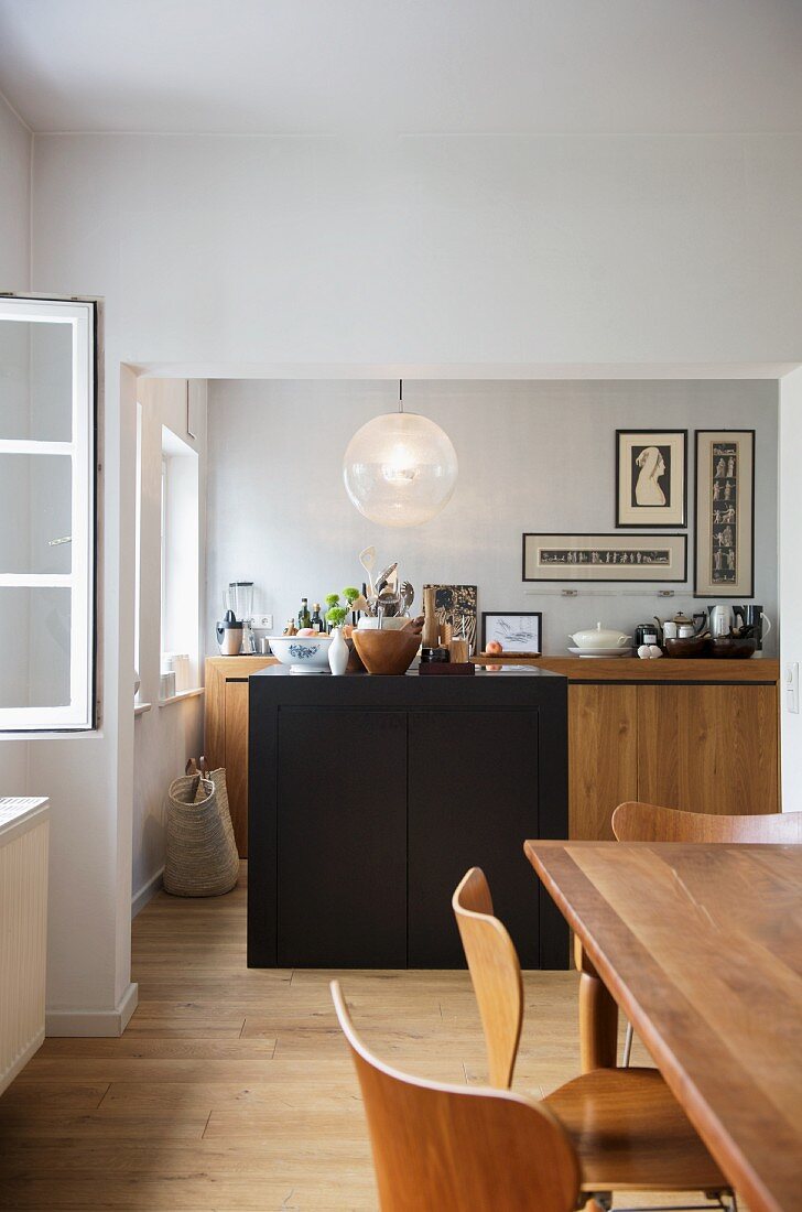 Wood with dark accents - view from dining area of cosy kitchen with island below spherical, retro glass light fitting