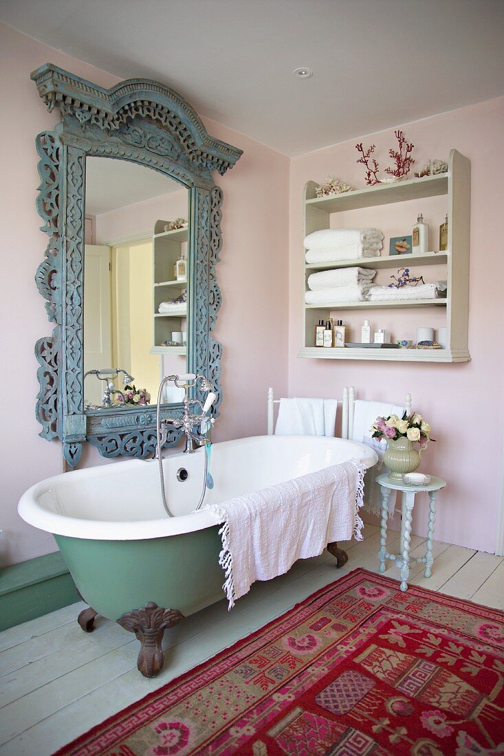 Altmodisches Bad im Shabby-Look mit freistehender Badewanne, antikem Spiegel und buntem Teppich auf Dielenboden