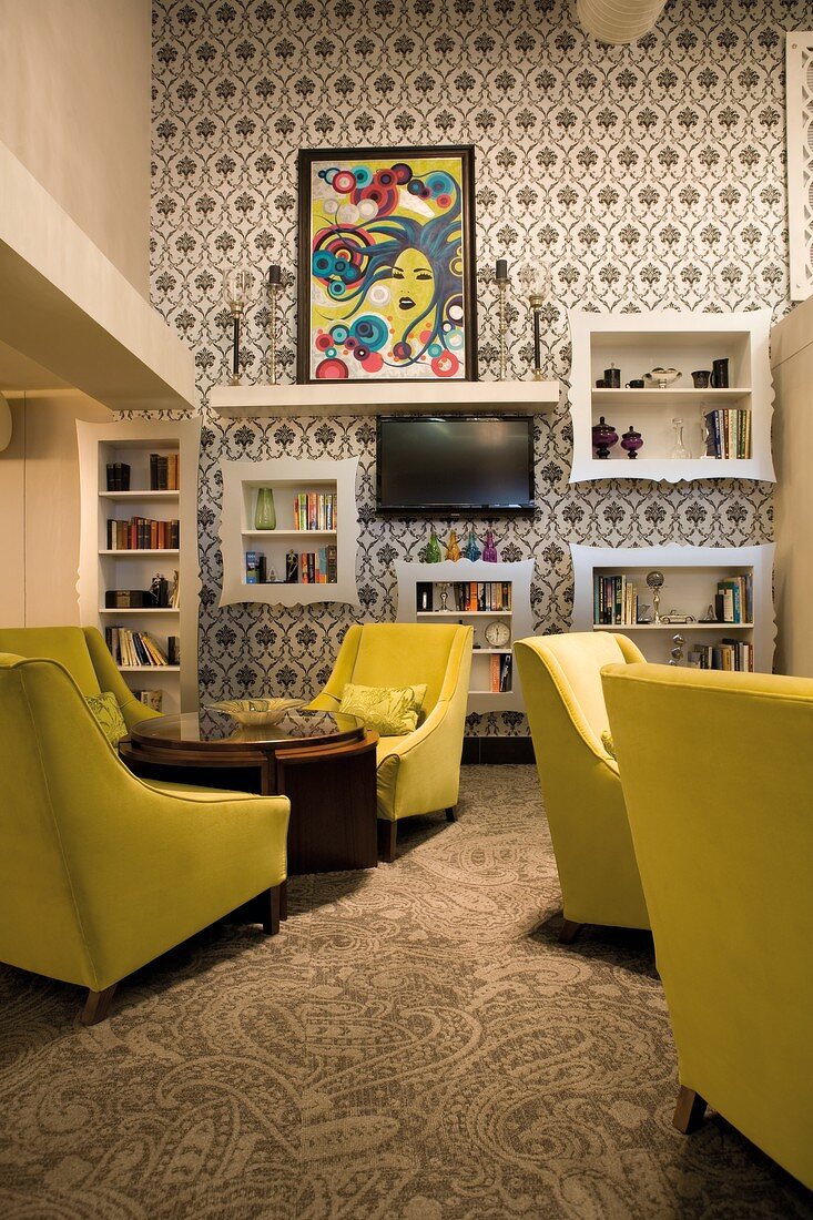 Groups of armchairs with yellow upholstery in lounge with ornate, retro-style black and white wallpaper