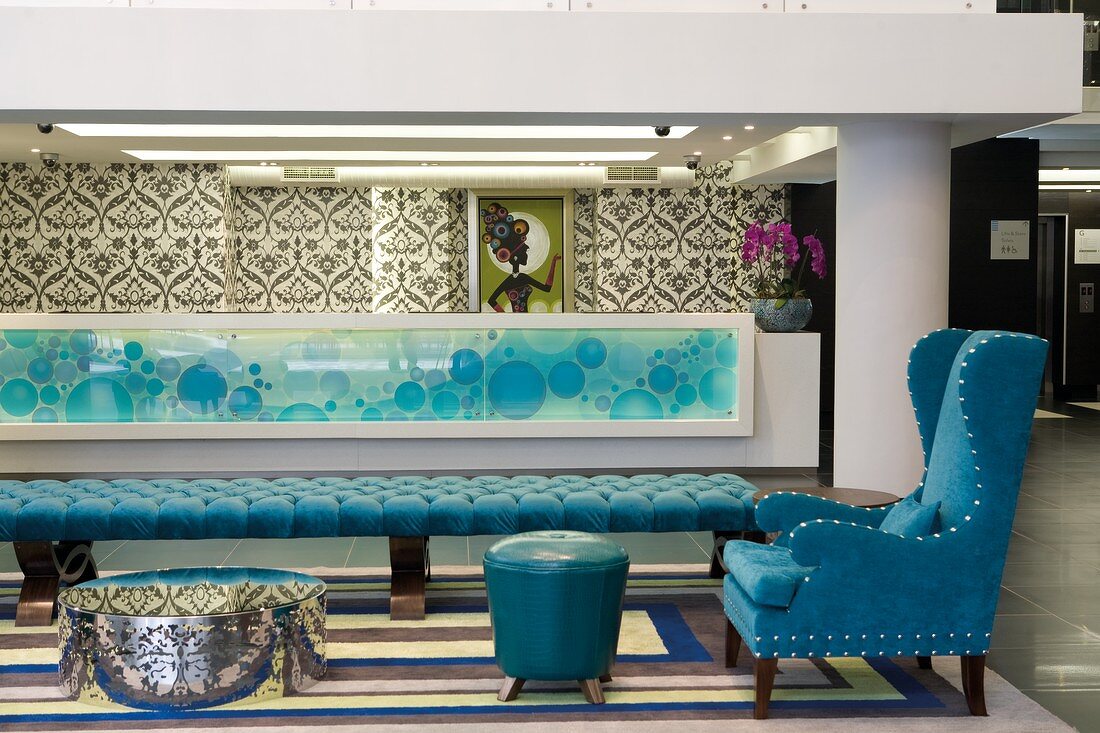 Loungebereich mit gepolsterter Liege und blauem Ohrensessel in Foyer mit langer Theke