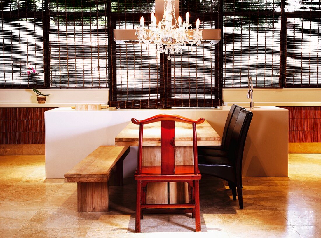 Moderne Designerküche mit schlichtem Sitzplatz vor dem Küchenblock, Kronleuchter und ausgefallener Holzstuhl als verspielte Elemente