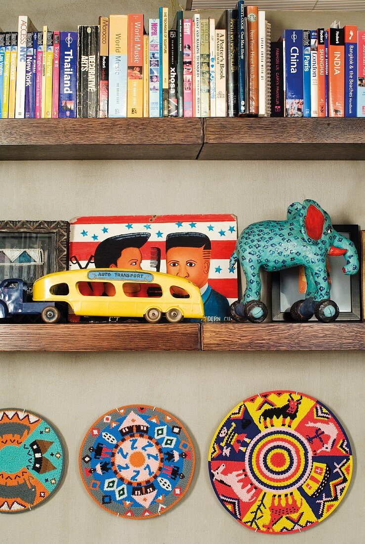 Bücher und Blechspielzeug auf Wandbord aus Holz und bemalte Teller an Wand befestigt