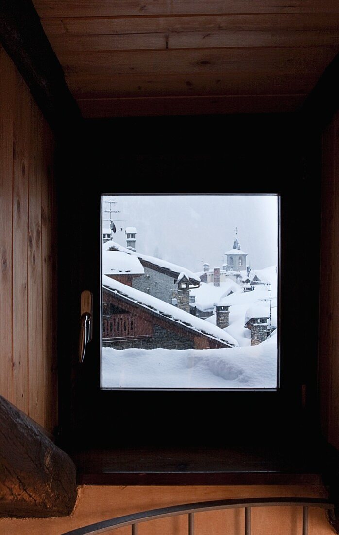 Blick durch das Treppenhausfenster auf verschneite Hausdächer