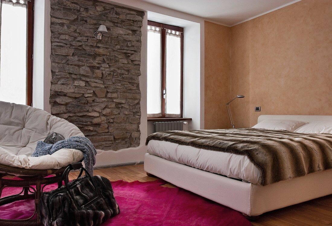 Schlafzimmer in warmen Erdtönen mit eingefasster, rustikaler Natursteinwand und einem Bettüberwurf mit Tierfellmotiv