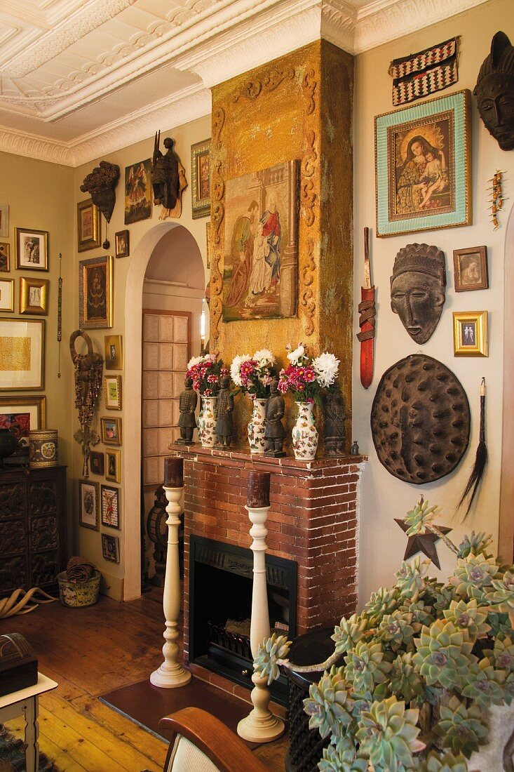 Wohnraum mit Stuckdecke und offenem Kamin, goldgerahmten Bildern und Ethno-Objekten an den Wänden