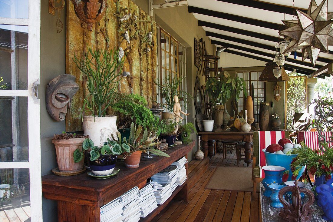 Grüne Veranda mit Sideboard aus Massivholz, einer blauen Vasensammlung und Pflanzen in Terrakottatöpfen