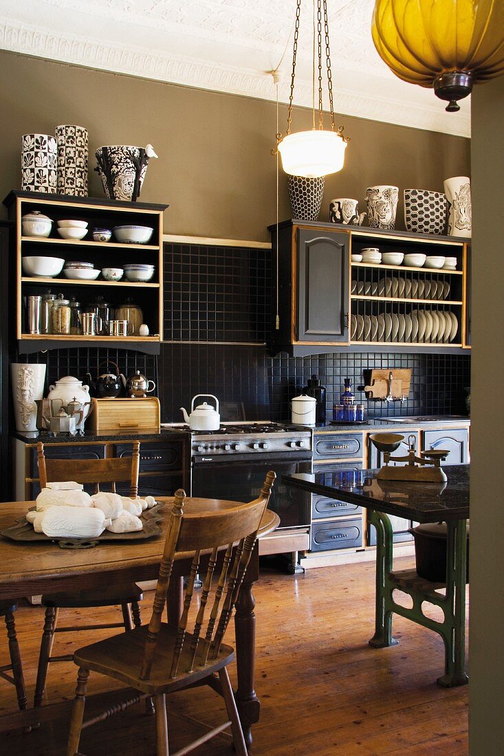 Olive green kitchen with antique furniture, art noveau ceiling lamp and a collection of black and white vases on the kitchen shelves