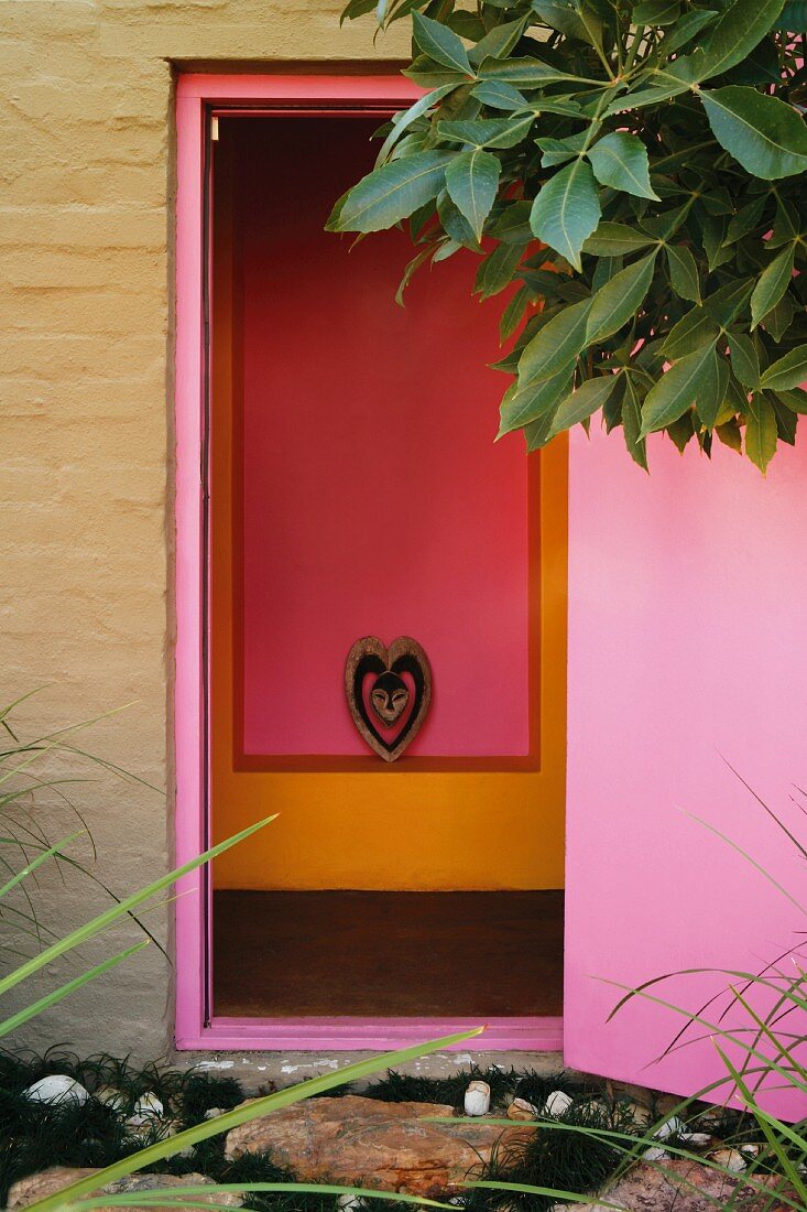 View from outside through a bright violet door of a pink and orange wall niche with an animal head inside a stylized heart