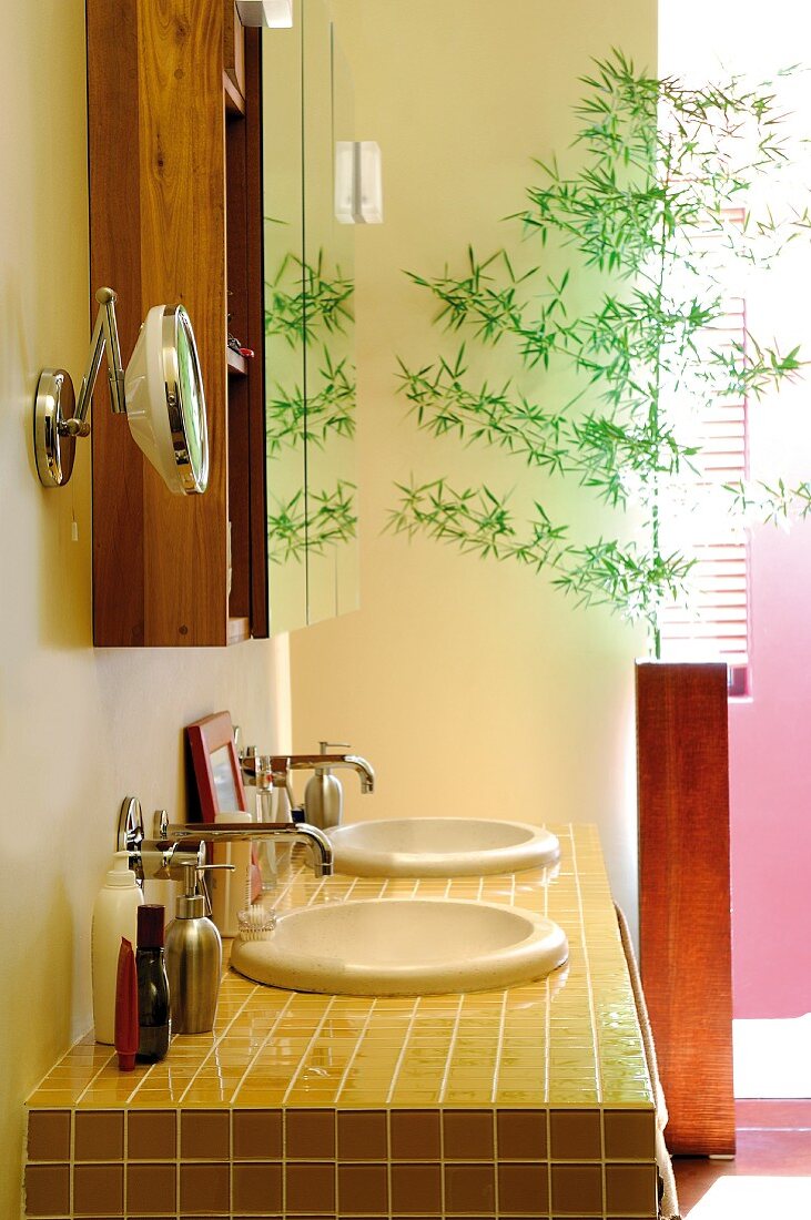 Gelb gefliester Waschtisch mit runden Becken und filigraner Zweig in moderner Bodenvase
