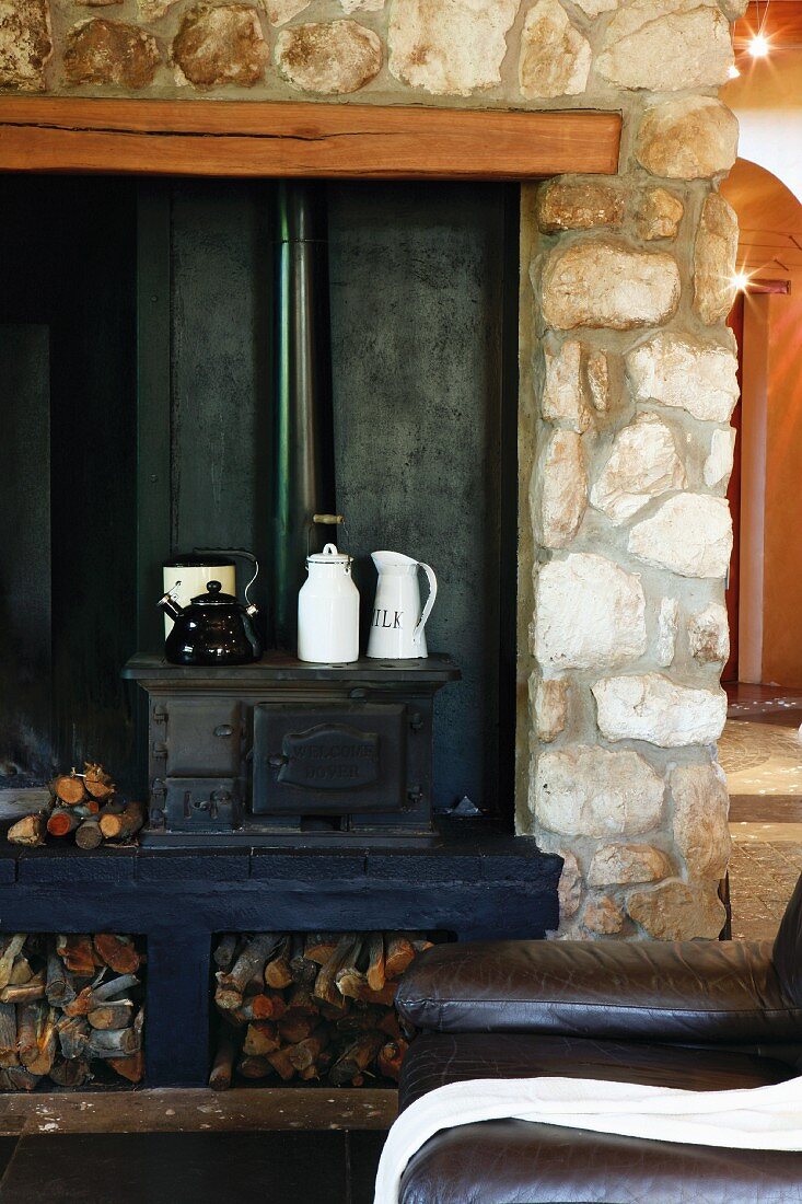 Jugs and kettle on small wood-burning stove in open fireplace with stone chimney breast