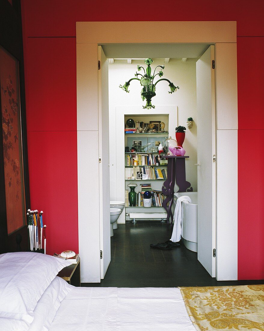 Blick von rot getöntem Schlafzimmer durch offene Flügeltür in modernes, weisses Bad