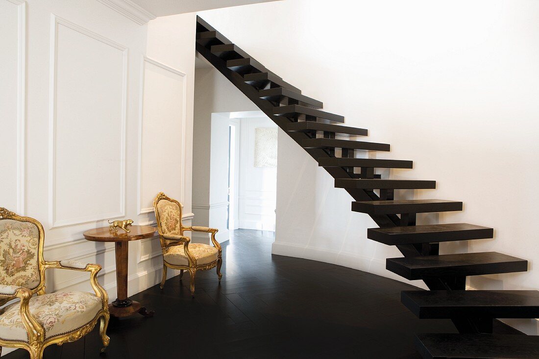 Purist, curved, wooden staircase without banisters in a traditional foyer with antique baroque armchairs