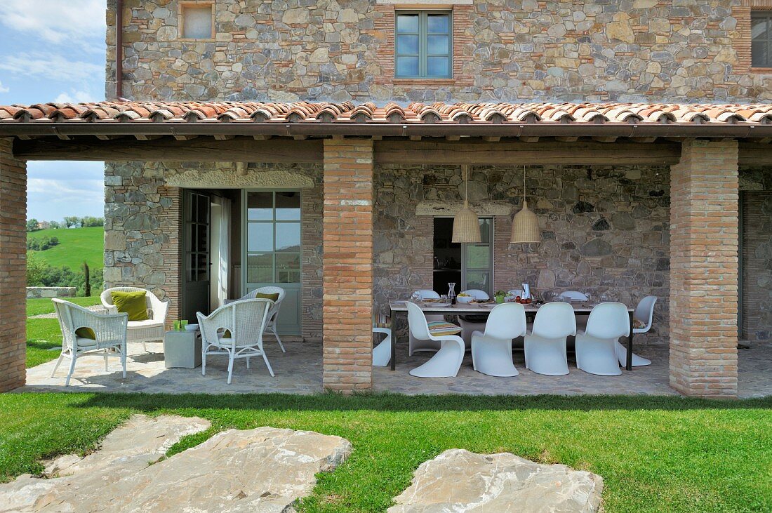 weiße Terrassenmöbel unter Vordach eines mediterranen Landhauses mit Natursteinfassade