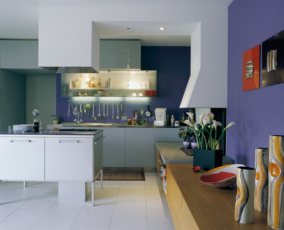 Designer Küchenblock mit Dunstabzug vor Küchenzeile in offenem Wohnraum mit Sideboard an blauer Wand