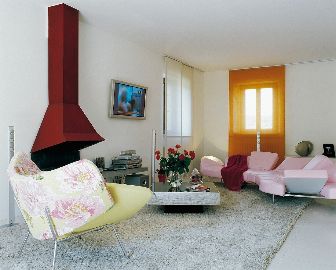 Rote Farbakzente in modernem Wohnraum - Designer Sessel mit Blumenmuster vor roter Kaminverkleidung und rosa Sofalandschaft auf hellem Flokatiteppich