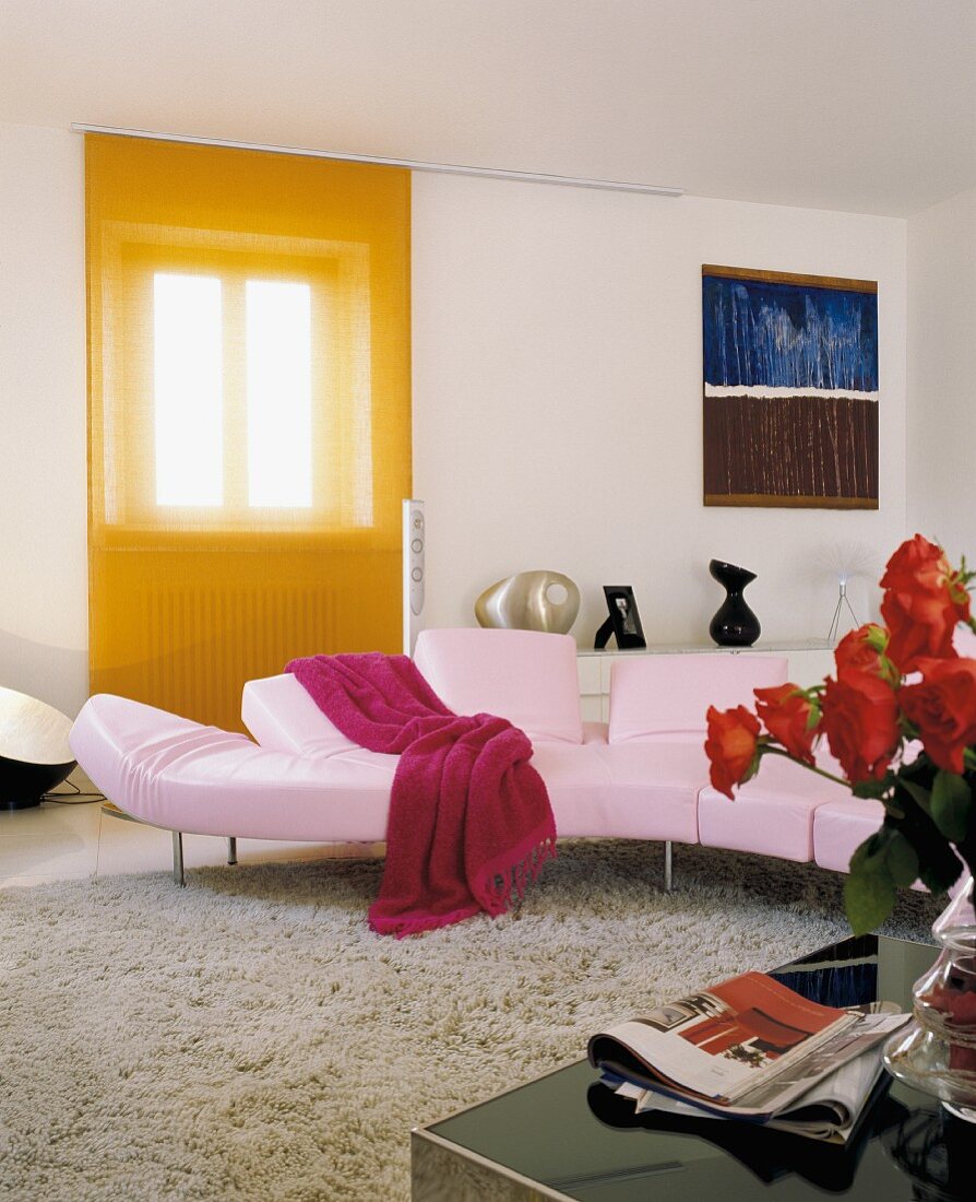 Rosa Sofa in modernem Wohnzimmer vor Fenster mit oranger, transparenter Schiebegardine