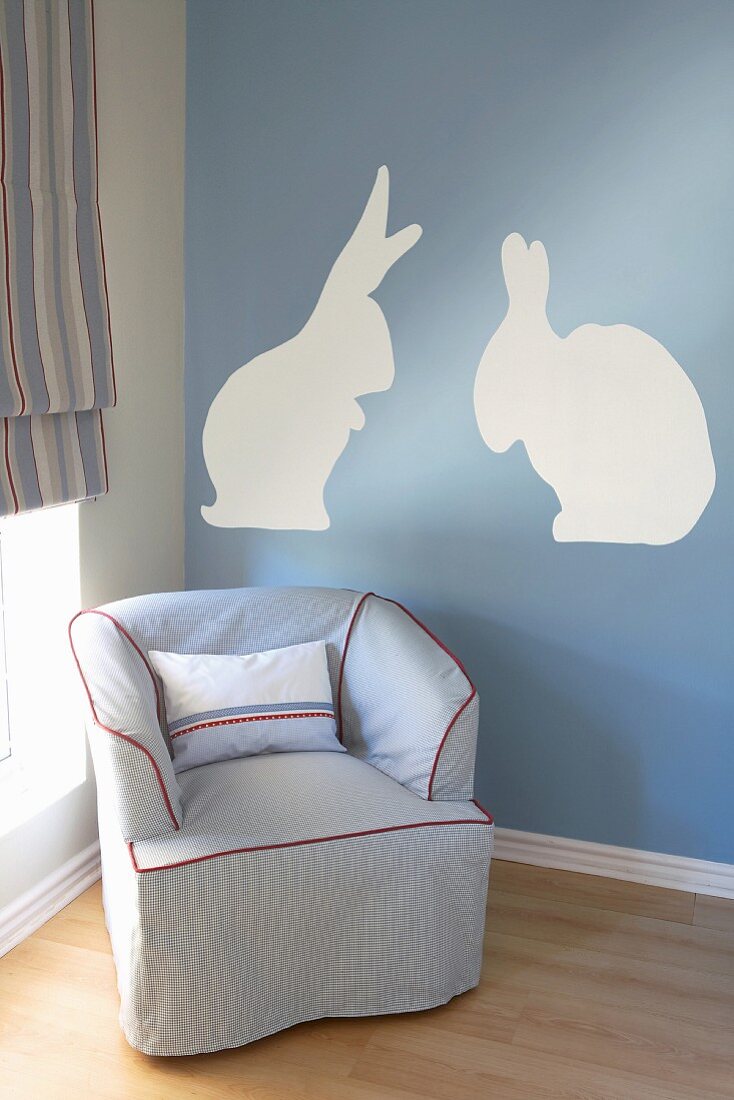 Upholstered armchair in front of wall painted with rabbit motif in nursery