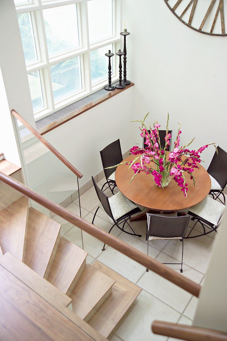 Dining area on white tiled floor in modern anteroom with wooden stairs