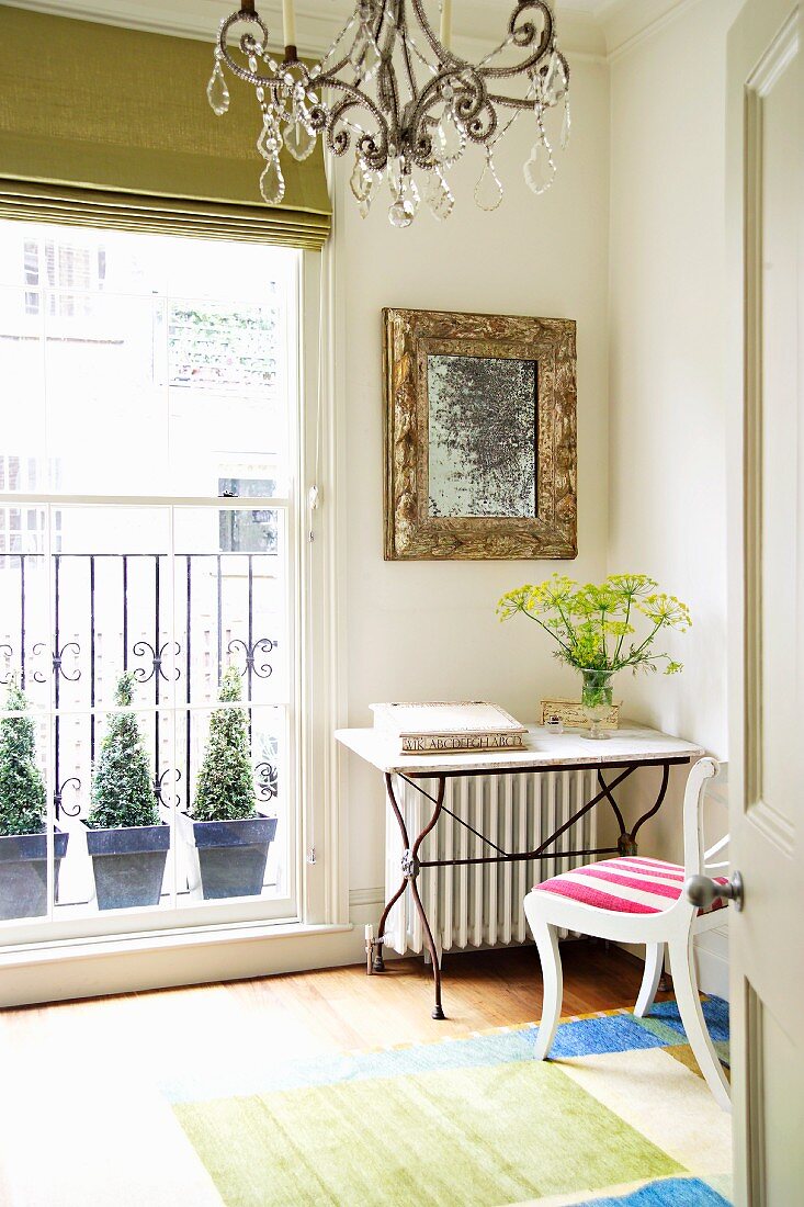 Table with metal frame and stone top in corner of room next to balcony door with view of potted plants