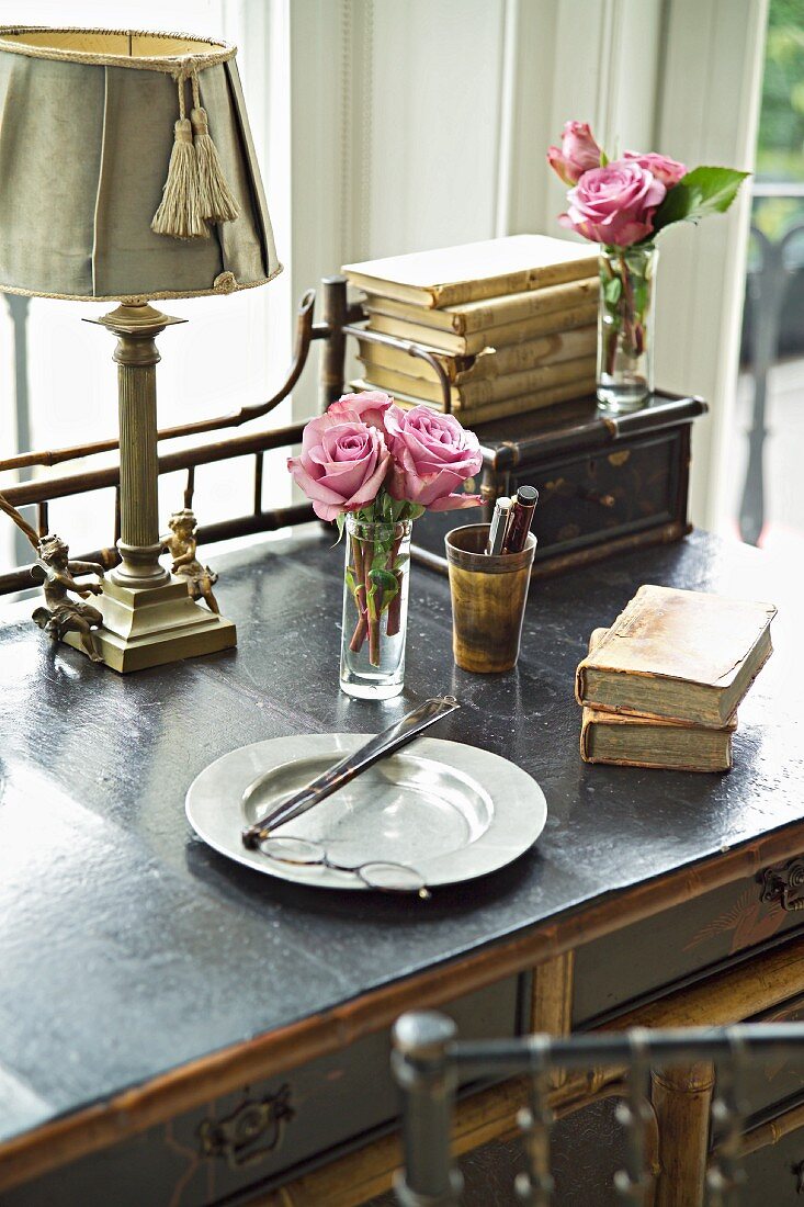 Frühstücksteller und antiquarische Bücher vor kleinem Rosenstrauß auf Schreibtisch