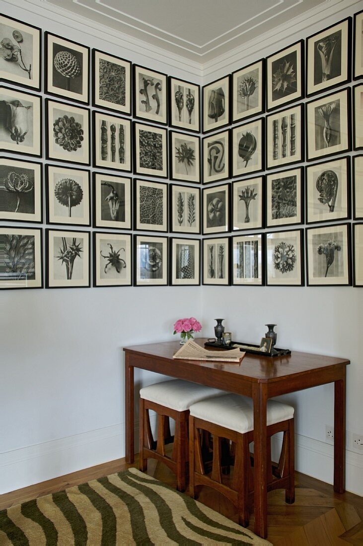 Gallery of black and white drawings above Biedermeier table with matching stools in corner of room