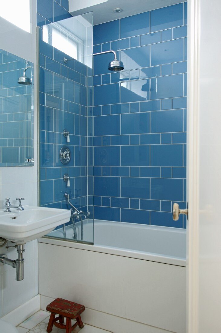 Corner of bathroom with bathtub and shower head against blue-tiled wall