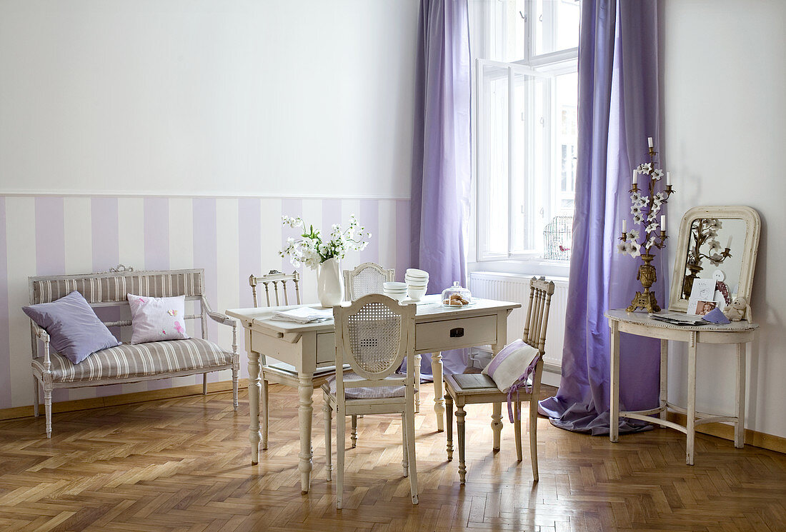 Alte französische Stühle um Holztisch im gustavianischem Stil und Sitzbank an Wand mit weissen und lila Streifen
