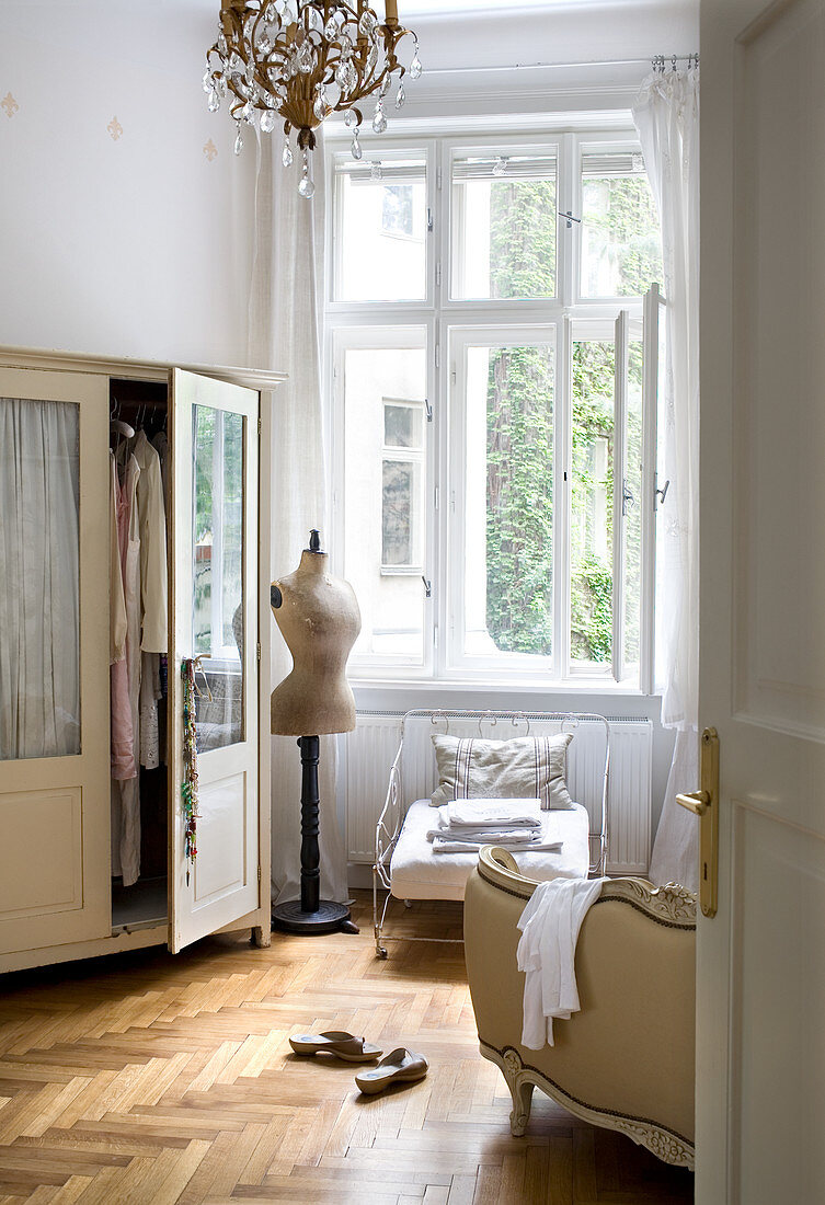 Wardrobe, tailors' dummy and old iron armchair in front of open window in bedroom of period apartment
