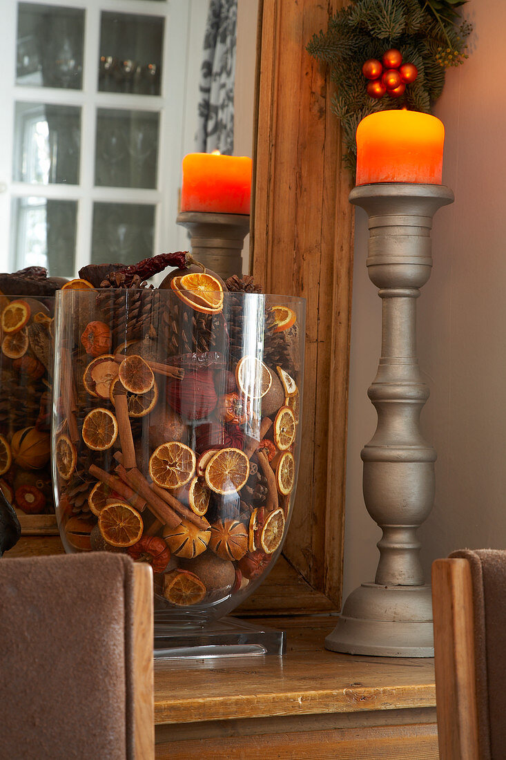 Dekorative Glasvase mit getrockneten Orangenscheiben und Zimtstangen neben gedrechseltem Kerzenständer