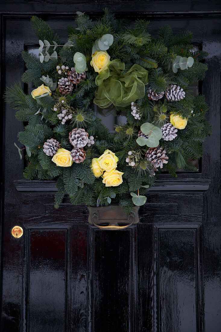 Kranzgebinde mit silbern besprühten Kieferzapfen und gelben Rosen als weihnachtliche Dekoration an alter Haustür