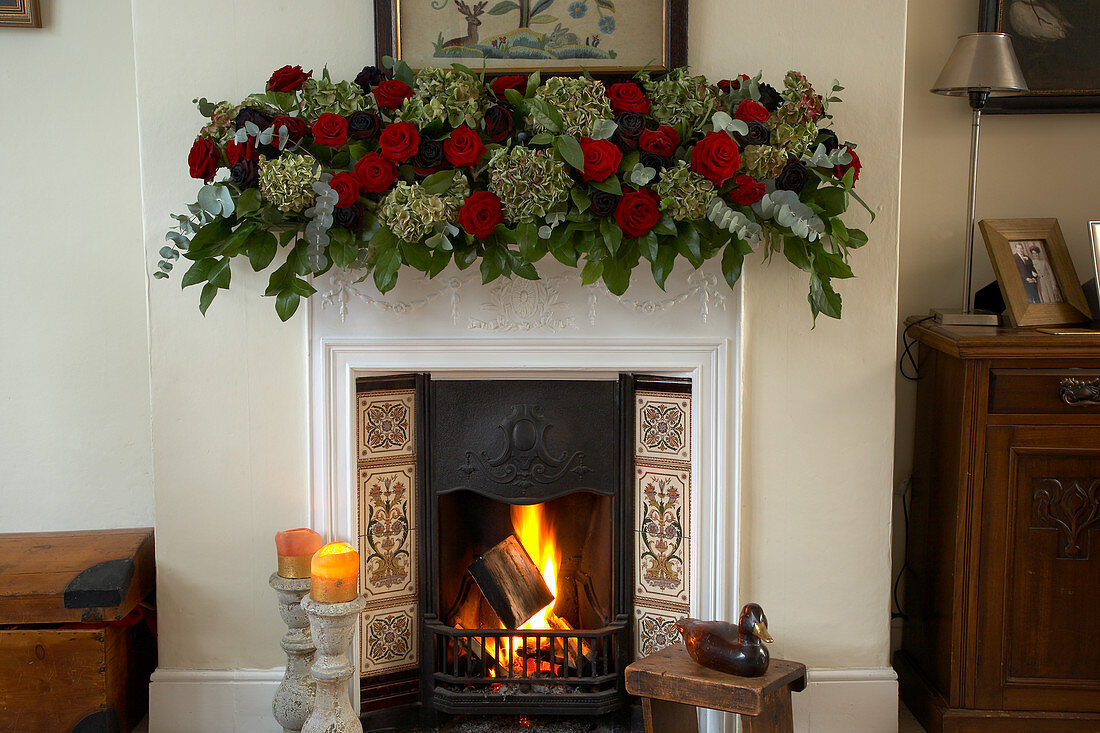 Prächtige Rosengirlande als englische Weihnachtsdekoration auf Kaminsims über brennendem Feuer
