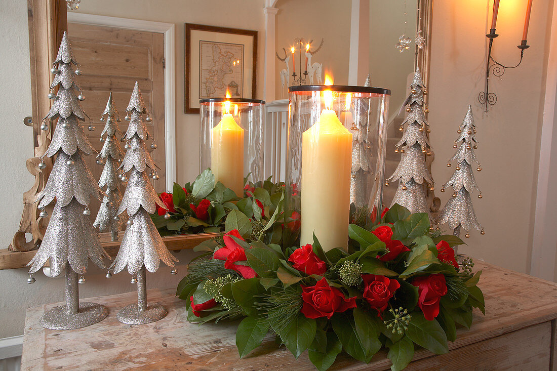 Brennende Kerze in Rosengesteck und stilisierte Tannenbäume aus Metall vor Garderobenspiegel