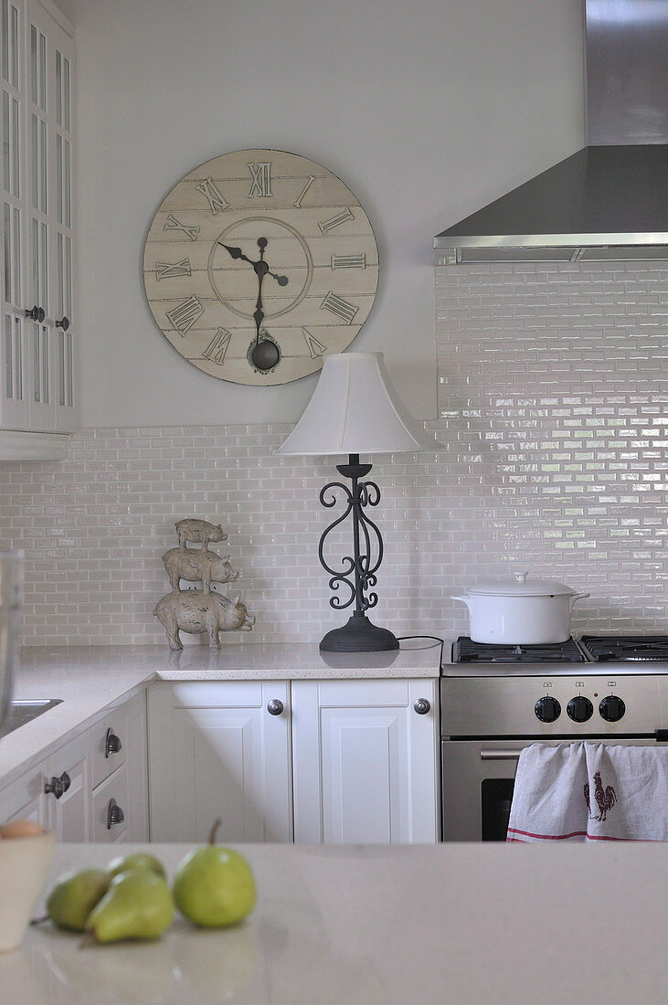 Nostalgic wall-mounted clock, wrought iron lamp base and pyramid of pigs decorating white, country house kitchen